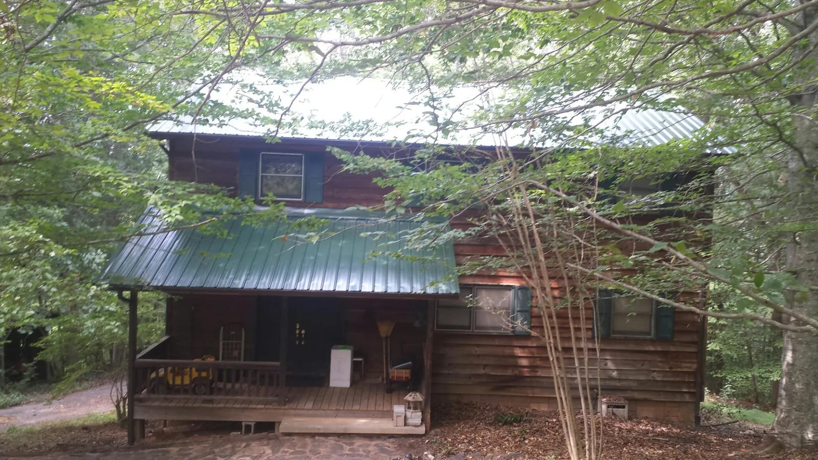 Green metal roof and covered porch on a log cabin in Conneautville