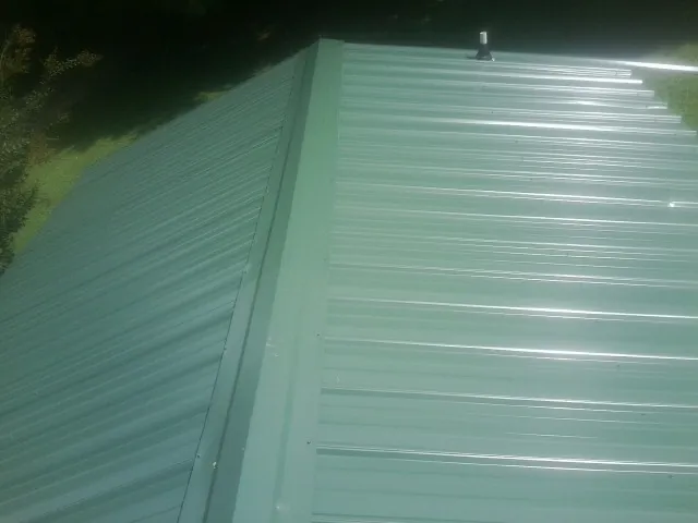 New green metal panels meeting at the ridge of a roof — Flat Roof Repair work by our crew in Conneautville