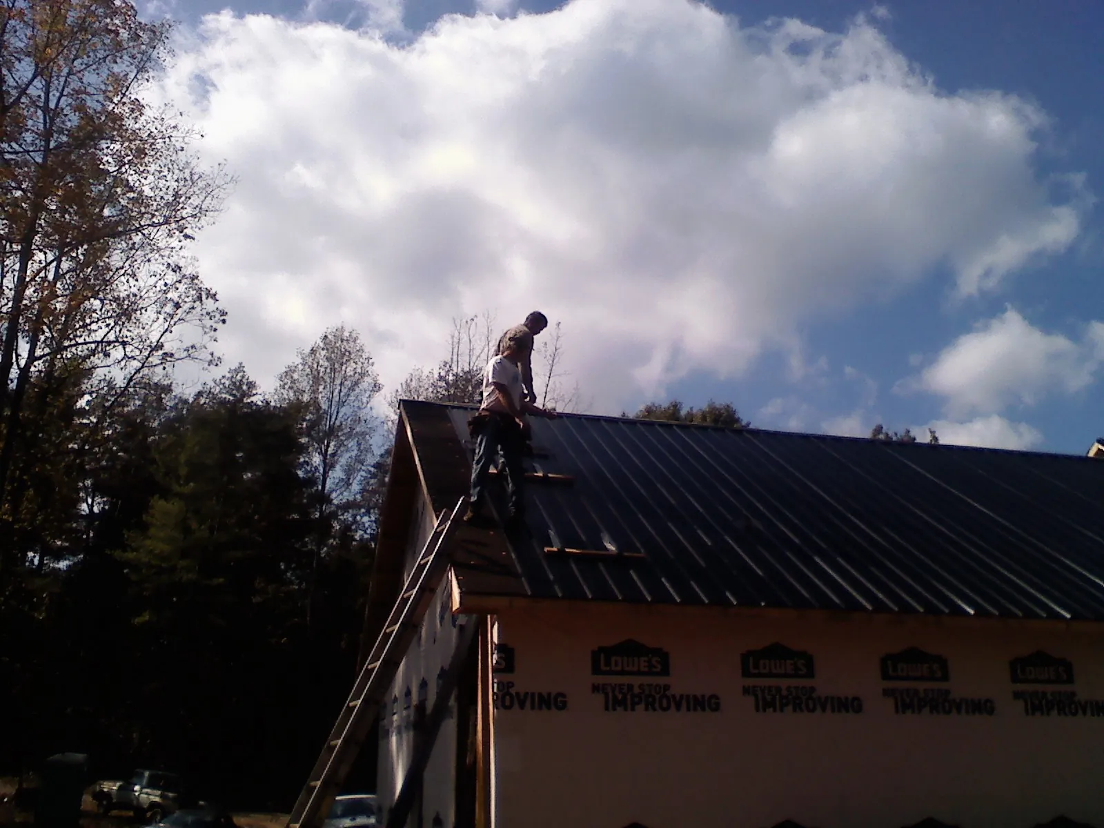 Roofer fastening dark metal panels high against a cloudy sky, from a Roof Inspection job in Conneautville