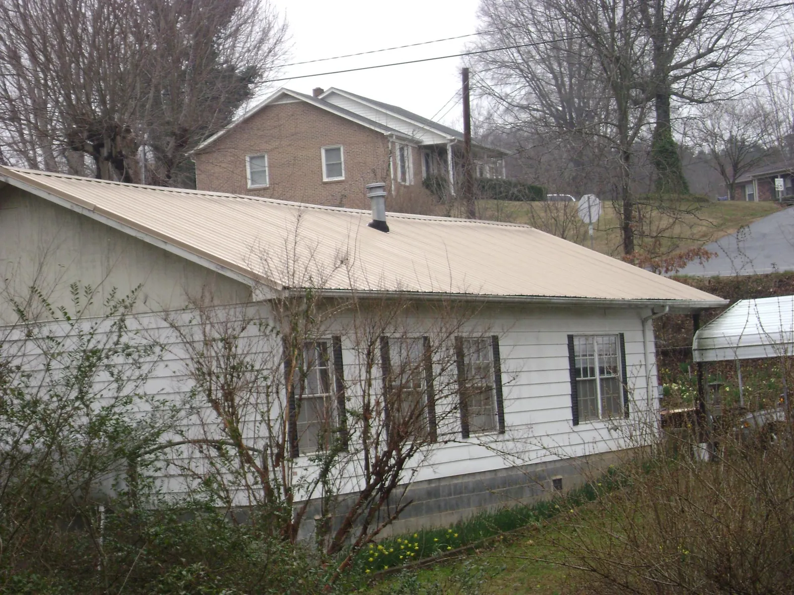 Tan metal roof on a white sided house set into a hillside — Commercial Roofing by Roofing Brothers in Conneautville