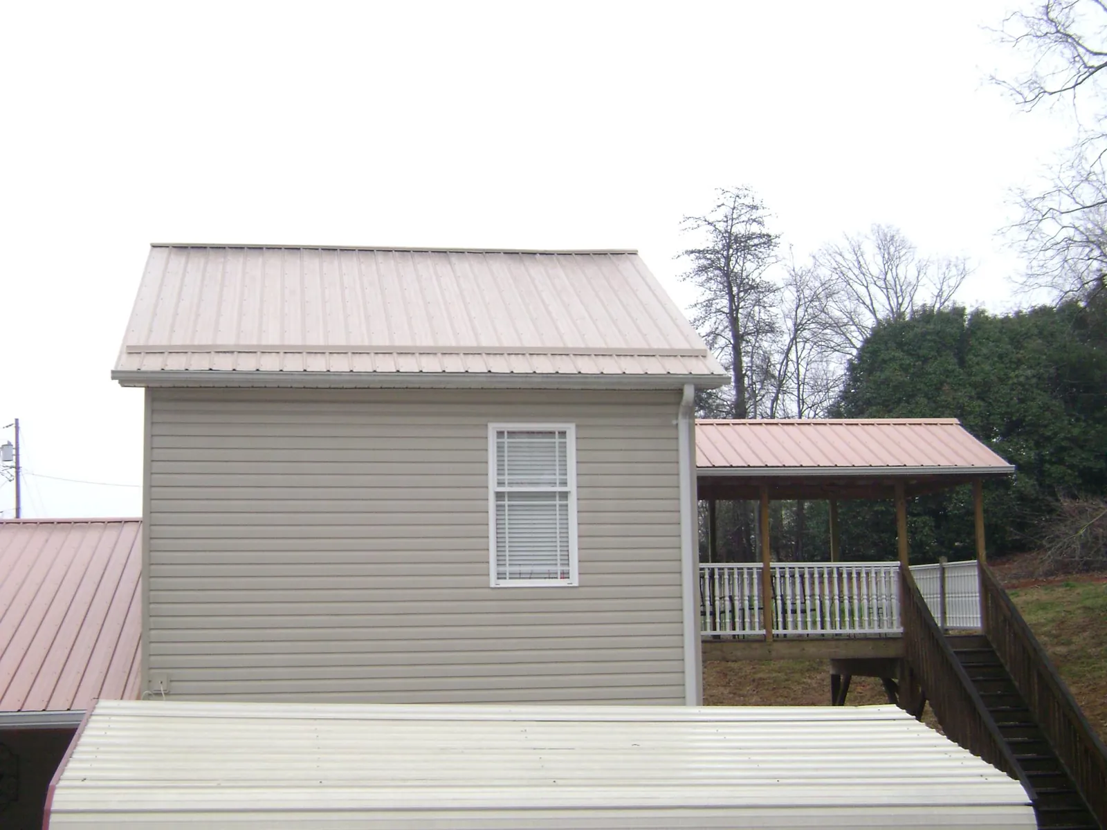 Tan metal roofs on a two story addition and attached porch, from a Roof Replacement job in Conneautville